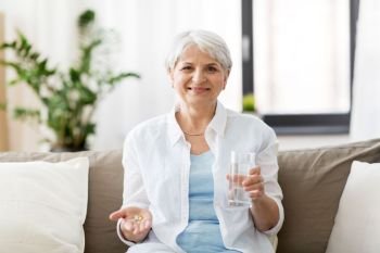 age, medicine, healthcare and people concept - senior woman with pills and glass of water at home. senior woman with water and medicine at home