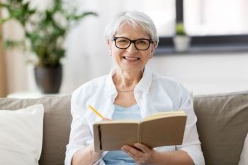 age, leisure and people concept - happy senior woman in glasses writing to notebook or diary at home. senior woman writing to notebook or diary at home