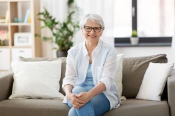 vision, age and people concept - portrait of happy senior woman in glasses sittin on sofa at home. portrait of happy senior woman in glasses at home