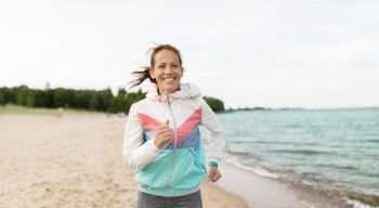 sport, technology and healthy lifestyle concept - smiling woman with fitness tracker running along beach. woman with fitness tracker running along beach