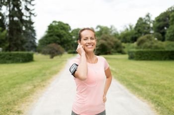 fitness, sport and healthy lifestyle concept - smiling woman with earphones wearing armband with smartphone at park and listening to music. woman with earphones and armband at park