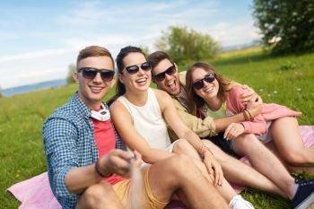 friendship, leisure and technology concept - group of happy smiling friends taking picture by selfie stick outdoors in summer. friends taking picture by selfie stick in summer