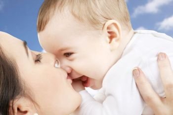 family and motherhood concept - happy smiling young mother kissing little baby over sky background. mother kissing baby over sky background