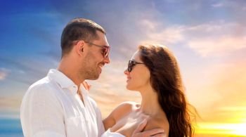 love, summer and relationships concept - happy smiling couple in sunglasses hugging over evening sky background. happy smiling couple in sunglasses hugging