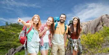 travel, tourism, hike and adventure concept - group of smiling friends with backpacks pointing finger to something over background of seychelles island. friends with backpacks over seychelles island
