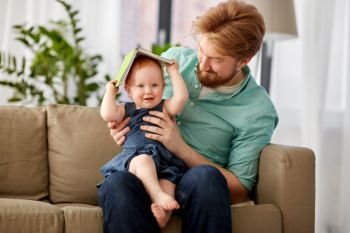 family, fatherhood and people concept - happy red haired father and little baby daughter playing with book at home. father and baby daughter playing with book at home