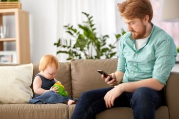 family, fatherhood and technology concept - red haired father with smartphone and little baby daughter playing with toy watering can at home. father with smartphone and baby playing at home