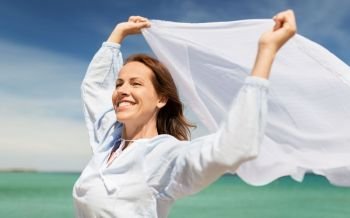 people and leisure concept - happy woman with shawl waving in wind on summer beach. happy woman with shawl waving in wind on beach