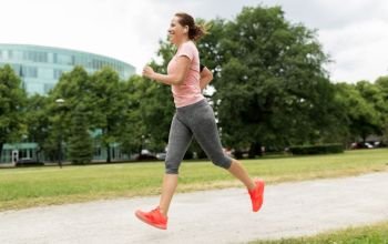 fitness, sport and healthy lifestyle concept - smiling woman with earphones running at park and listening to music. woman with earphones running at park