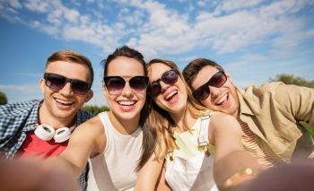 leisure, people and friendship concept - happy teenage friends taking selfie outdoors in summer. happy friends taking selfie outdoors in summer