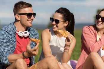 friendship, leisure and food concept - group of smiling friends eating pizza at picnic in summer. happy friends eating pizza at picnic in summer