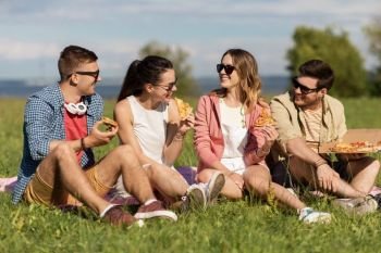 friendship, leisure and food concept - group of smiling friends eating pizza at picnic in summer park. friends eating pizza at picnic in summer park
