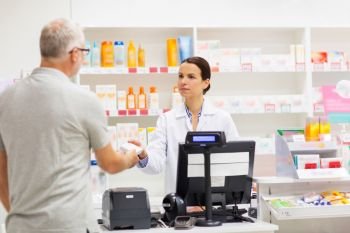 medicine, pharmaceutics, health care and people concept - apothecary giving drug to senior man customer at drugstore. apothecary showing drug to senior man at pharmacy