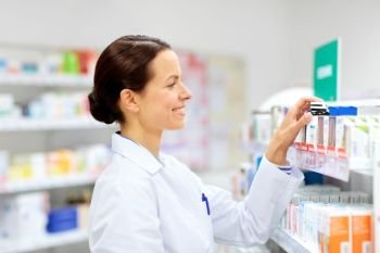 medicine, pharmaceutics, healthcare and people concept - happy female apothecary taking drug from shelf at pharmacy. happy female apothecary with drug at pharmacy