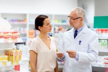medicine, healthcare and people concept - senior apothecary with prescription talking to female customer at pharmacy. apothecary and woman with prescription at pharmacy