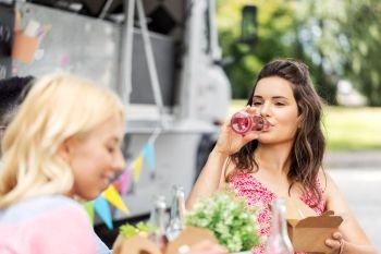 leisure and people concept - female friends drinking lemonade and eating at food truck. friends drinking lemonade and eating at food truck