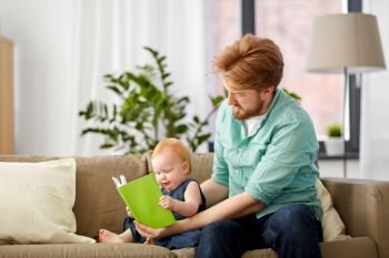 family, fatherhood and people concept - happy red haired father and little baby daughter with book at home. father and baby daughter with book at home