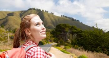 adventure, travel, tourism, hike and people concept - smiling young woman with backpack over big sur hills of california background. smiling woman with backpack over big sur hills