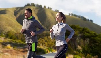 fitness, sport, people and healthy lifestyle concept - happy couple running over big sur hills and road background in california. happy couple running outdoors