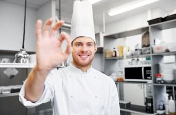 cooking, profession and people concept - happy male chef cook in toque at restaurant kitchen showing ok hand sign. happy chef at restaurant kitchen showing ok sign