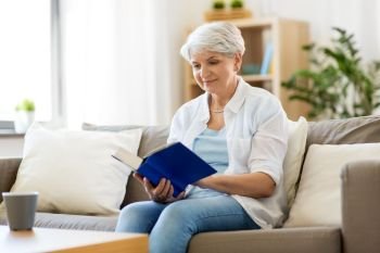 age, leisure and people concept - happy smiling senior woman reading book at home. happy smiling senior woman reading book at home