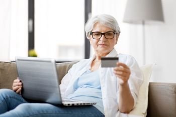 technology, online shopping and people concept - happy senior woman in glasses with laptop computer and credit or bank card at home. senior woman with laptop and credit card at home