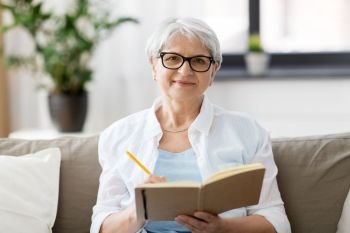 age, leisure and people concept - happy senior woman in glasses writing to notebook or diary at home. senior woman writing to notebook or diary at home