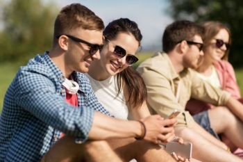 friendship, technology and leisure concept - group of smiling friends with smartphone in summer. happy friends with smartphone ourtdoors in summer