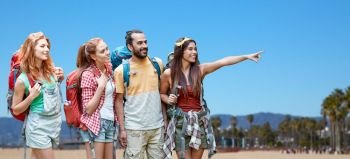 travel, tourism, hike and adventure concept - group of smiling friends with backpacks pointing finger to something over venice beach background in california. group of friends with backpacks over venice beach