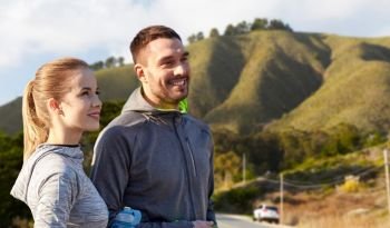 fitness, sport and people concept - smiling couple with bottles of water over big sur hills background in california. couple of sportsmen with water over big sur hills