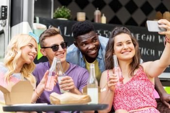 leisure and people concept - happy young friends with food and non alcoholic drinks and taking selfie at food truck. happy young friends taking selfie at food truck