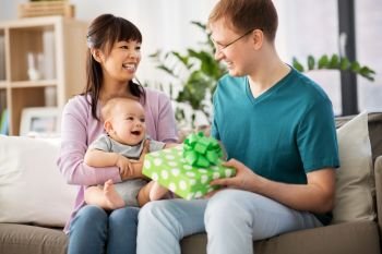 family, parenthood and fathers day concept - happy mother with baby boy giving birthday present to father at home. mother with baby giving birthday present to father