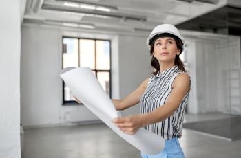 building, architecture and construction business concept - businesswoman or architect in helmet with blueprint at office room. architect in helmet with blueprint at office room