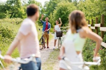 people, leisure and lifestyle concept - happy young friends with fixed gear bicycles in summer waving hands. happy friends with fixed gear bicycles in summer