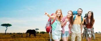 travel, tourism, hike and adventure concept - group of smiling friends with backpacks pointing finger to something over animals in african savannah background. friends with backpacks over african savannah