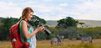 travel, tourism and photography concept - happy young woman with backpack and camera photographing over zebras in african savannah background. woman with backpack and camera over savannah