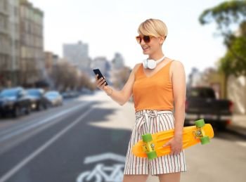 sport, leisure and skateboarding concept - smiling teenage girl in sunglasses with short modern cruiser skateboard and smartphone over san francisco city street background. teenage girl with skateboard and smartphone