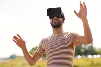 technology, virtual reality, entertainment and people concept - smiling man with vr headset or 3d glasses playing video game outdoors. smiling man in virtual reality headset outdoors