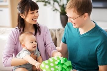 family, parenthood and fathers day concept - happy mother with baby boy giving birthday present to father at home. mother with baby giving birthday present to father