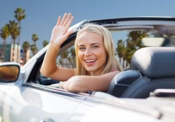 travel, road trip and people concept - happy young woman in convertible car waving hand over venice beach background in california. happy young woman in convertible car waving hand