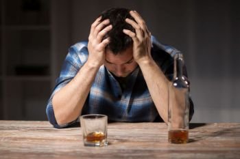 alcoholism, alcohol addiction and people concept - male alcoholic with bottle and glass drinking whiskey at night. alcoholic with bottle drinking whiskey at night