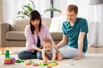 family, parenthood and people concept - happy mother, father and baby boy playing toy blocks at home. happy family with baby boy playing at home