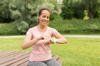 sport and technology concept - smiling woman with smart watch or fitness tracker in park. woman with smart watch or fitness tracker in park