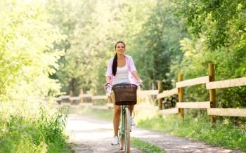 people, leisure and lifestyle - happy young woman riding fixie bicycle with basket at summer park. woman riding bicycle with basket at summer park