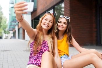 friendship, leisure and technology concept - smiling teenage girls taking selfie by smartphone on street in summer city. teen girls taking selfie by smartphone in city