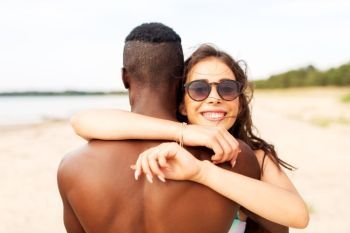 love, summer holidays and people concept - happy mixed race couple hugging on beach. happy mixed race couple hugging on summer beach
