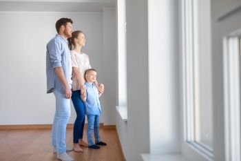 family, people and real estate concept - happy mother, father and little son looking through window at new home or apartment. happy family with child at new home or apartment
