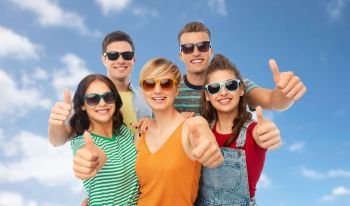 friendship, summer and people concept - group of happy smiling friends in sunglasses showing thumbs up over blue sky and clouds background. happy friends showing thumbs up