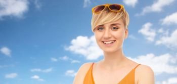 summer fashion, style and eyewear concept - portrait of happy smiling teenage girl with sunglasses over blue sky and clouds background. portrait of smiling teenage girl with sunglasses