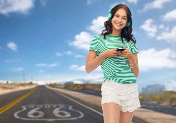 music, travel and tourism concept - happy teenage girl in headphones with smartphone over route 66 background. teenage girl in phones with smartphone on route 66
